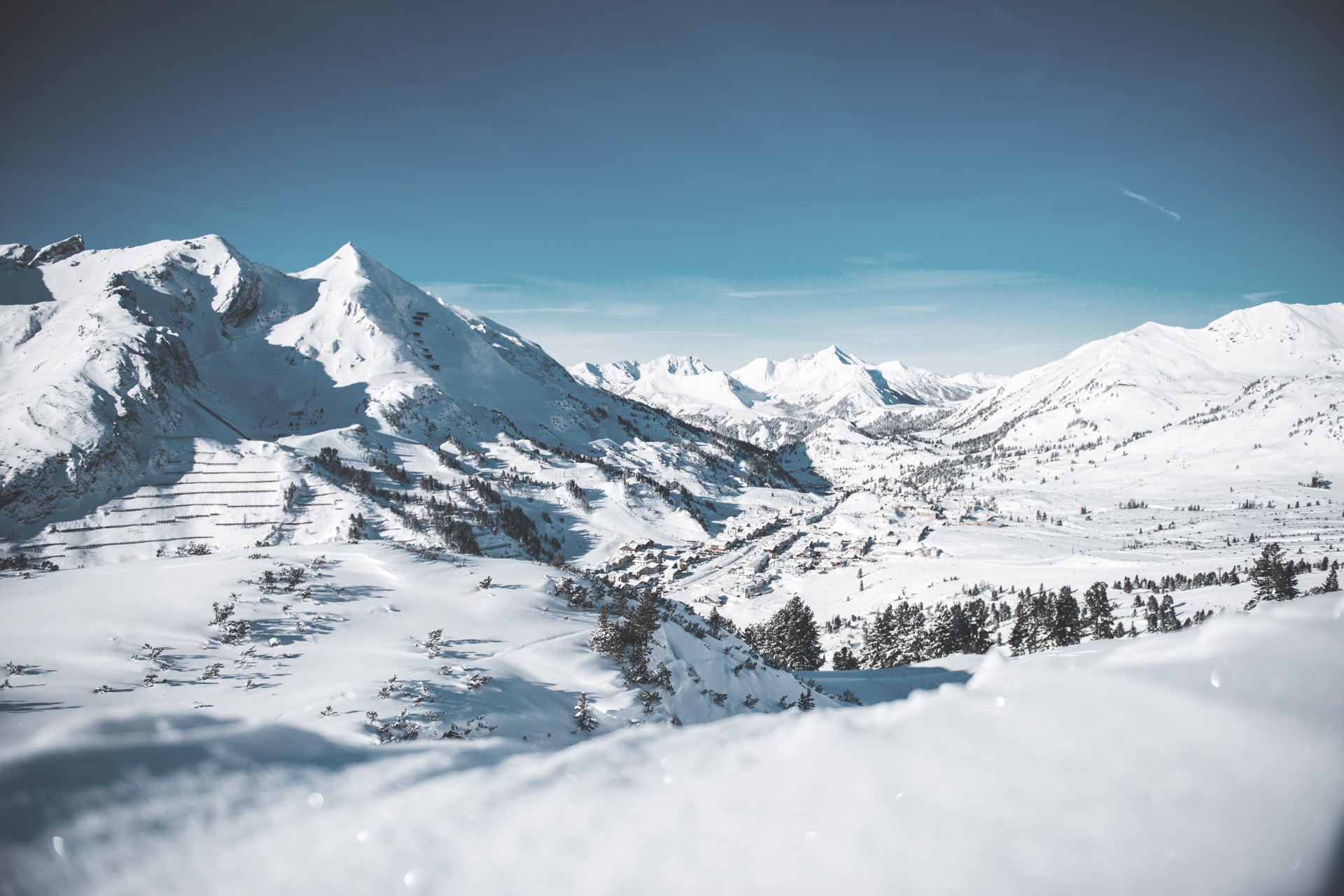 A serene winter landscape: pristine white snow blankets rolling hills and rugged mountains under a clear blue sky.