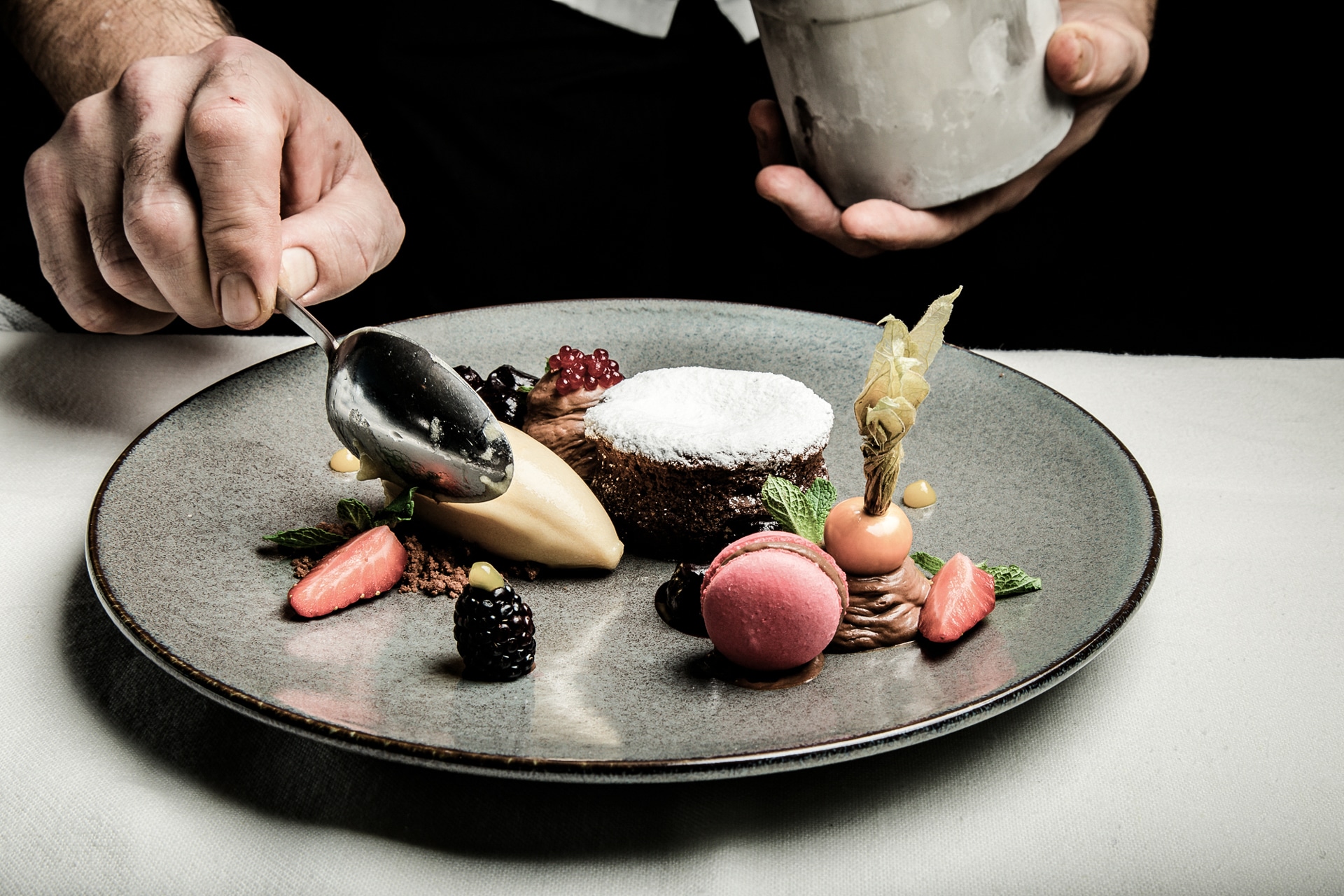 A chef putting the finishing touch on a gourmet dessert platter with delicate chocolate sauce, showcasing an artistic arrangement of a chocolate cake, a quenelle of ice cream, macarons, and fresh berries.