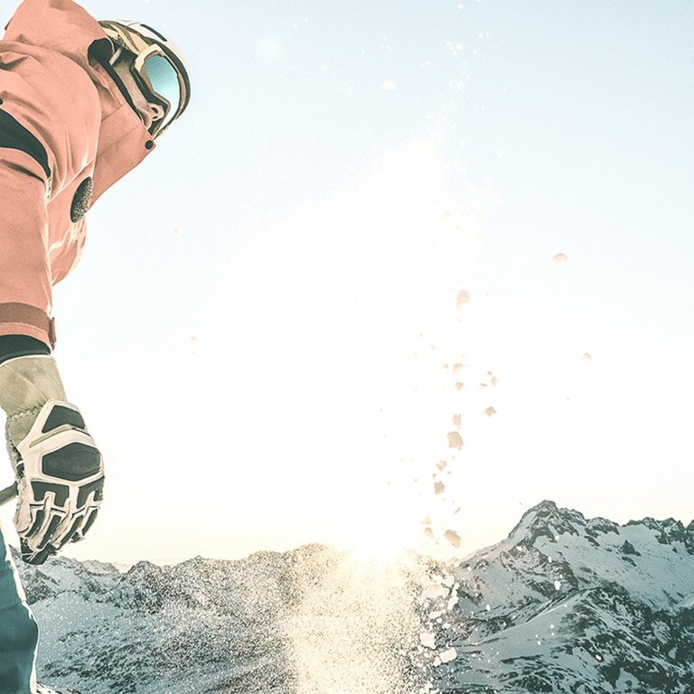 Ein Skifahrer steht auf einem schneebedeckten Berggipfel, genießt die Wintersonne und ist bereit für eine abenteuerliche Abfahrt.