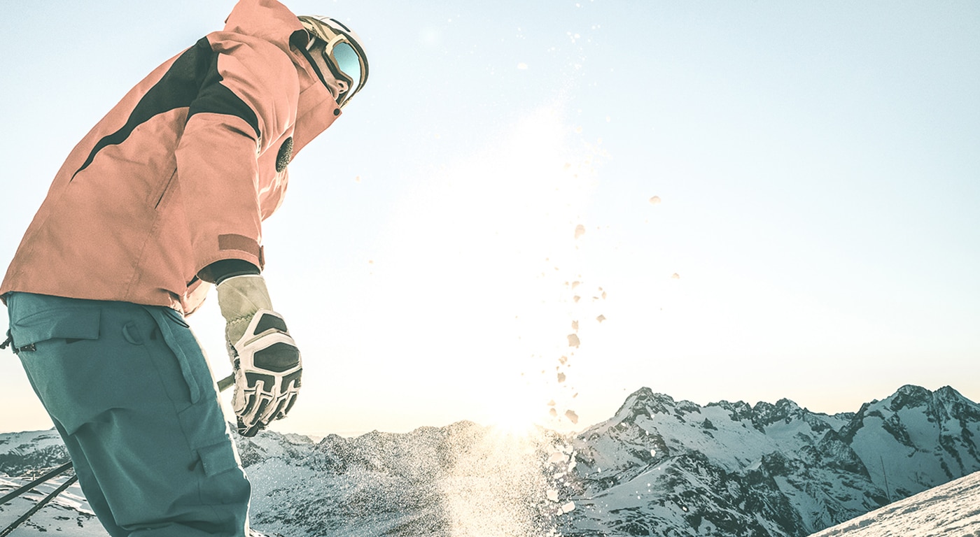 Ein Skifahrer steht auf einem schneebedeckten Berggipfel, genießt die Wintersonne und ist bereit für eine abenteuerliche Abfahrt.