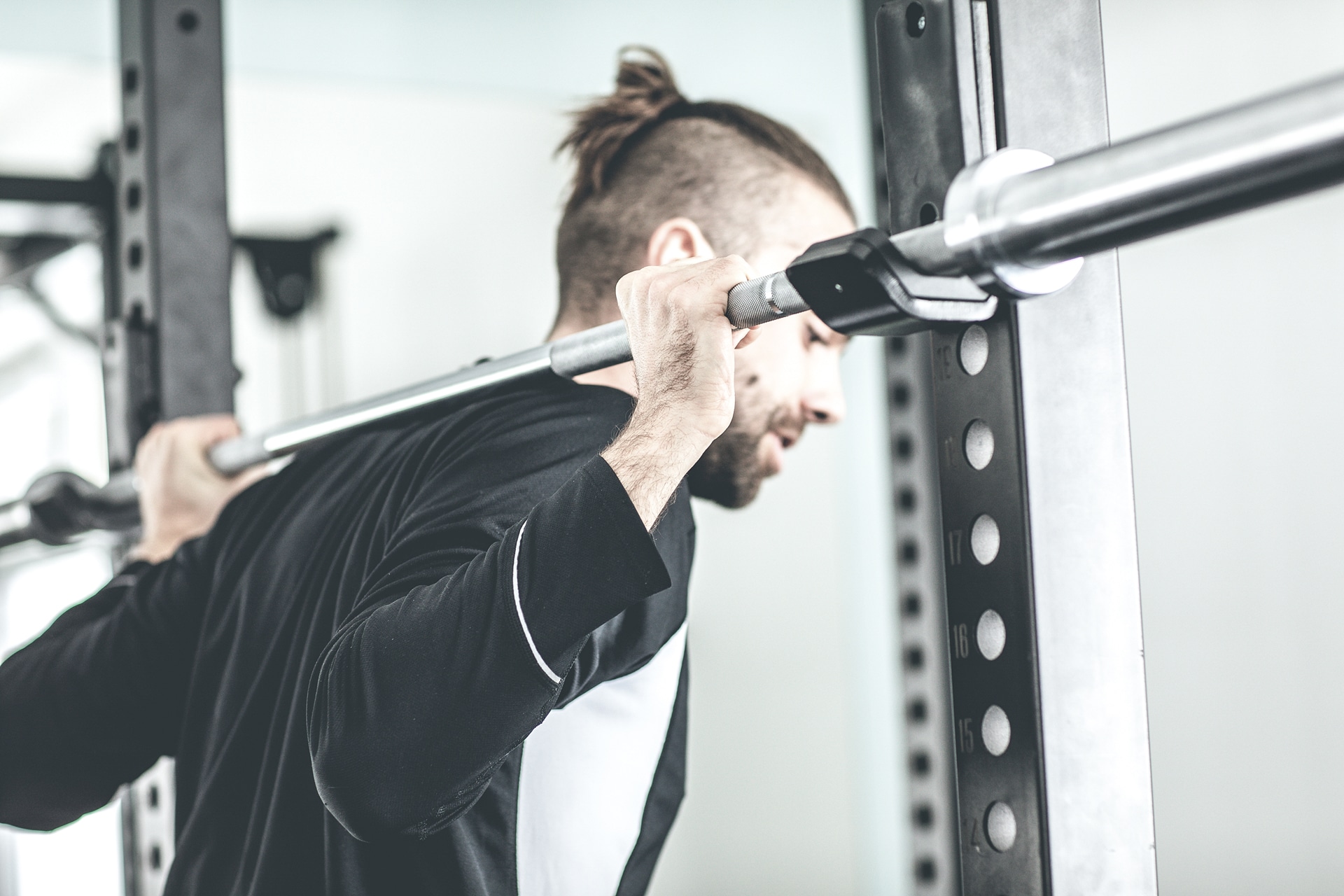 Mann macht in einem Fitnessstudio Kniebeugen mit Gewichten, konzentriert sich auf Krafttraining.